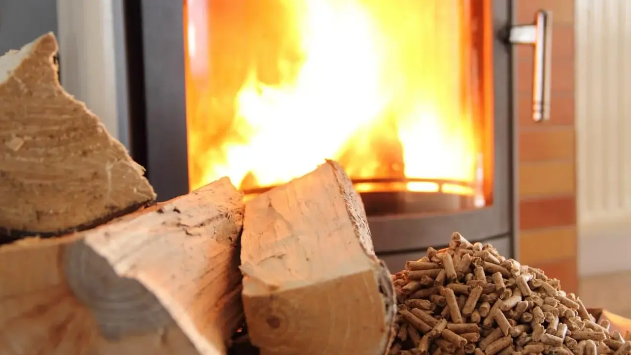 Bûches et granulés de bois prêts pour le chauffage au bois, avec un poêle crépitant en arrière-plan.