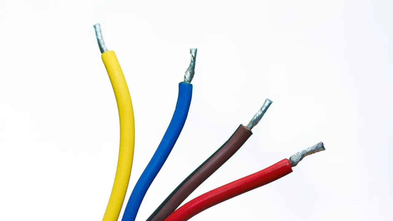 Faisceau de fils électriques colorés : jaune, bleu, marron et rouge. Un fil noir est caché parmi eux, prêt à transporter l'électricité.