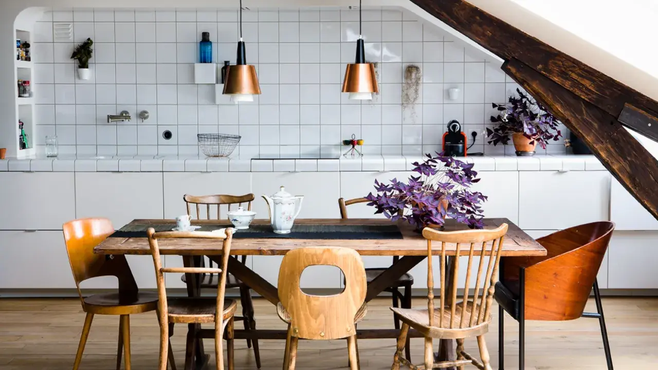 Une cuisine ouverte sur salle à manger avec un îlot central, des chaises en bois et des suspensions cuivrées.