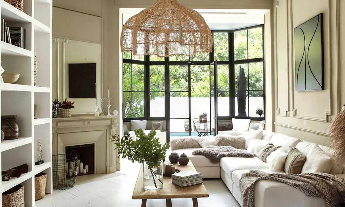 Salon lumineux au style bohème chic maison, avec canapé blanc, suspensions en rotin, cheminée et grandes fenêtres donnant sur le jardin.