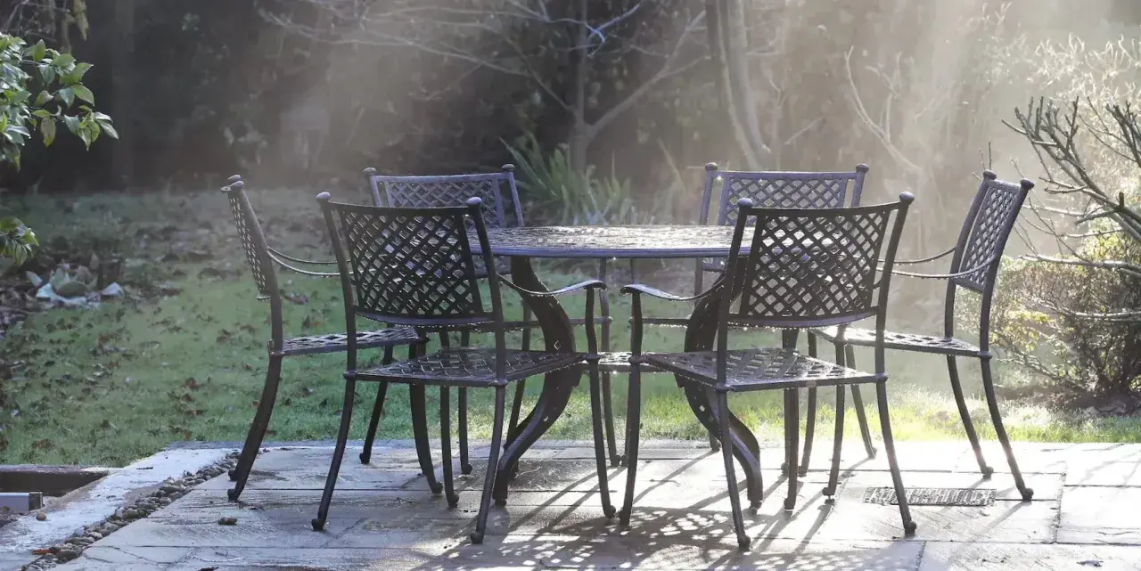 Un ensemble de mobilier de jardin résistant aux intempéries, une table et quatre chaises en métal, est mouillé par la rosée matinale.