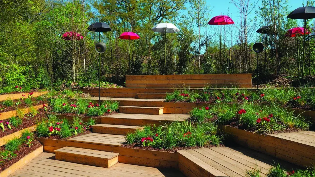 Aménagement de jardins avec terrasses en bois, parterres fleuris et parasols colorés.