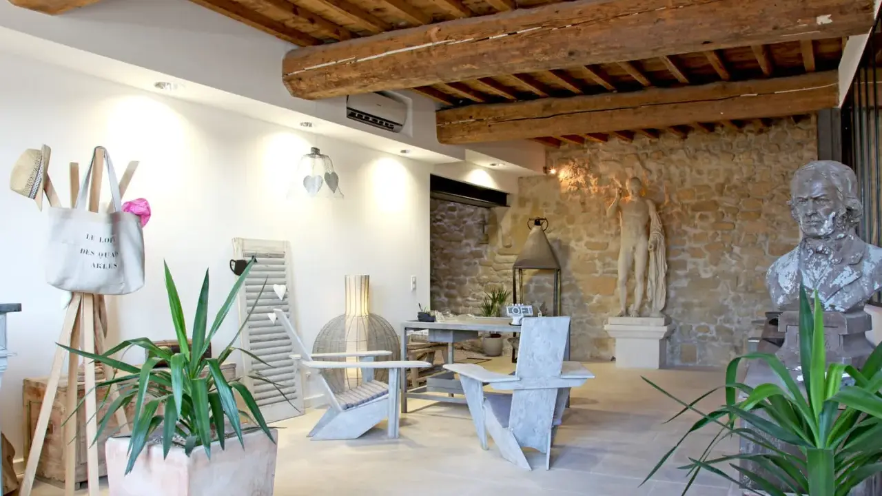 Salon moderne avec poutre apparente. Deux fauteuils en bois, une table, des plantes et des statues ornent cet espace chaleureux.