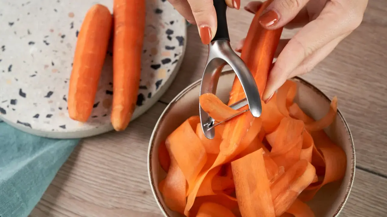 Des carottes épluchées tombent en rubans dans un bol. Une astuce pour comment conserver les carottes : les préparer ainsi pour une cuisson rapide.