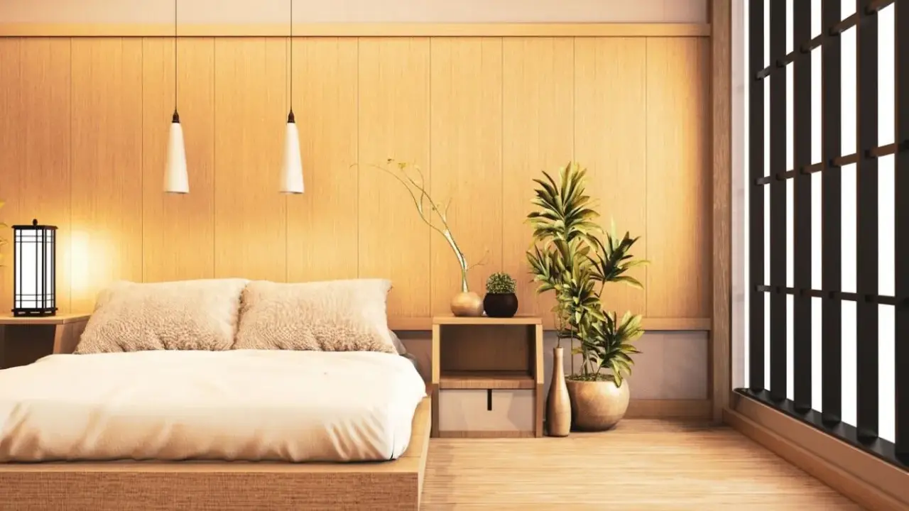 Une chambre style japonais épurée avec un lit bas en bois, des coussins douillets, des plantes vertes et une fenêtre aux persiennes sombres.