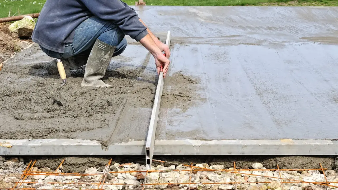 Un ouvrier ajuste le coffrage d'une dalle en béton frais avec une règle de maçon.