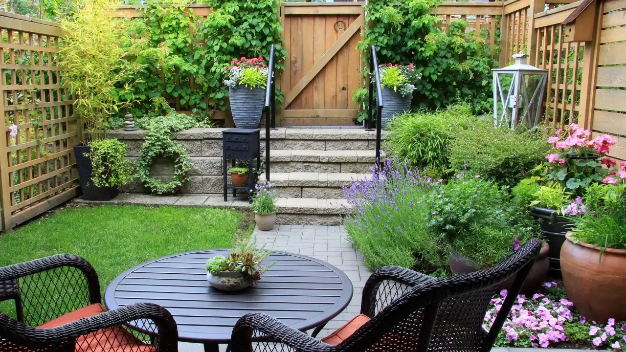 Un petit jardin aménagé avec une table, des chaises, des plantes et une porte en bois.