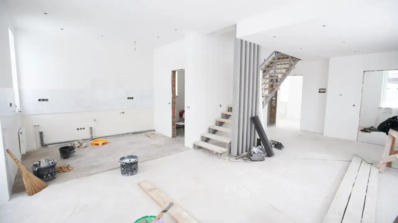 Chantier en cours pour rénover ma maison : escalier, seaux de peinture, balai et matériaux au sol.