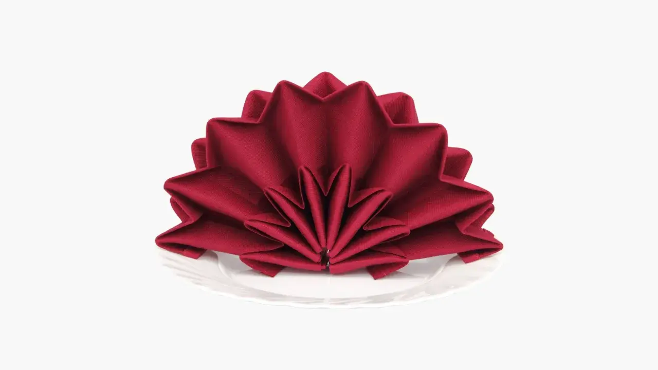 Une serviette rouge bordeaux pliée en éventail sur une assiette blanche. Un pliage serviette simple et beau pour une table élégante.