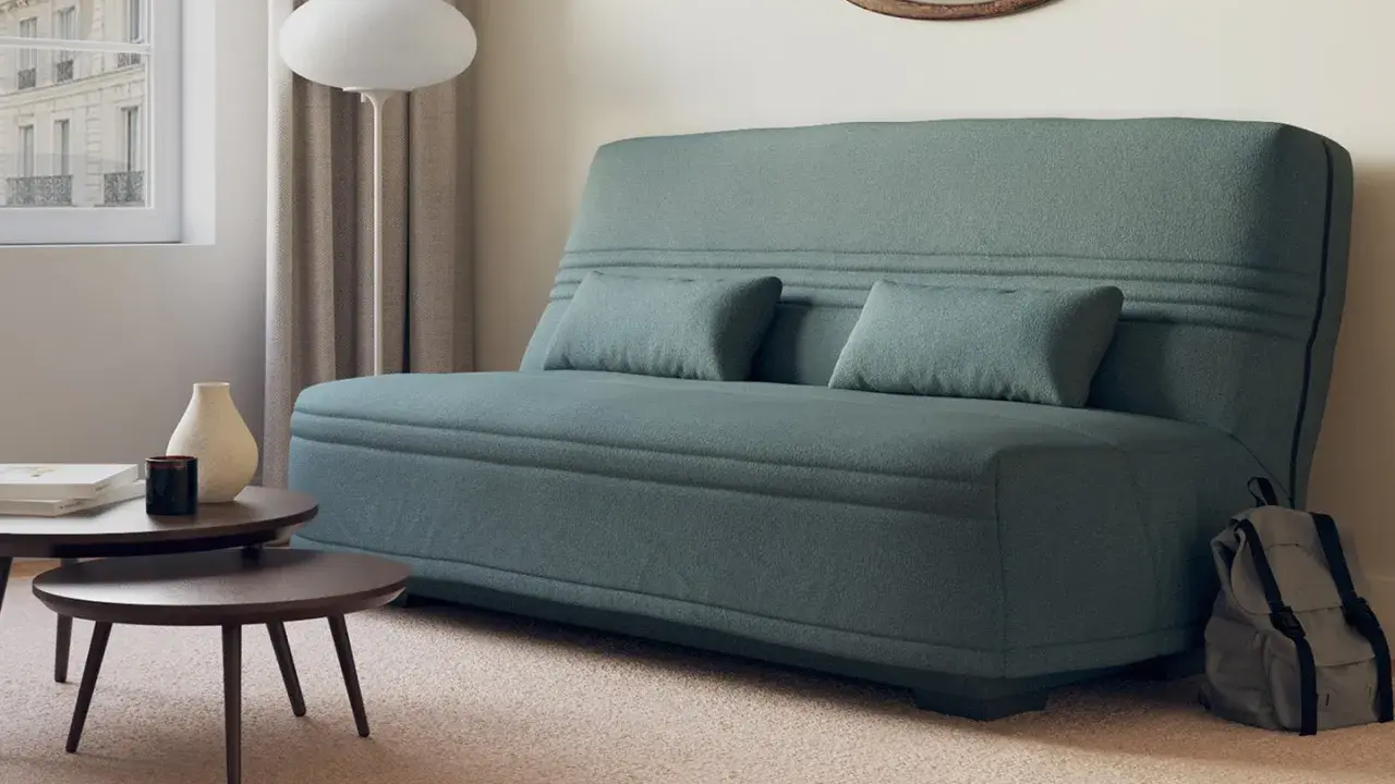 Canapé bz ou clic clac bleu canard, avec coussins, près d'une fenêtre et de tables basses. Parfait pour un petit espace.