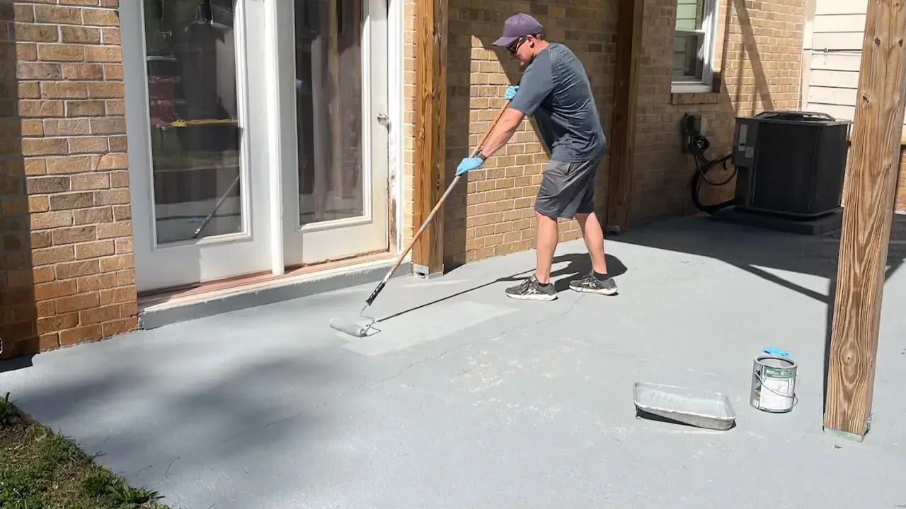 Homme appliquant une peinture sur mur béton extérieur avec un rouleau. Le sol de la terrasse est en cours de rénovation.