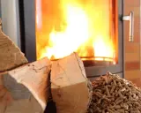 Bûches et granulés de bois prêts pour le chauffage au bois, avec un poêle crépitant en arrière-plan.