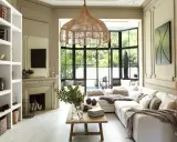 Salon lumineux au style bohème chic maison, avec canapé blanc, suspensions en rotin, cheminée et grandes fenêtres donnant sur le jardin.