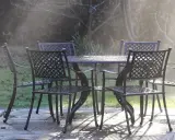 Un ensemble de mobilier de jardin résistant aux intempéries, une table et quatre chaises en métal, est mouillé par la rosée matinale.
