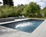Aménagement paysager d'une piscine creusée avec terrasse en pierre, deux chaises bleues et un hamac invitant à la détente.