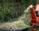Une brouette remplie de broyat de bois, projeté par une déchiqueteuse orange.