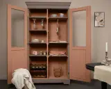 Armoire vitrée avec un relooking meuble 2 couleurs : gris anthracite et rose poudré. Elle contient vaisselle, verres, bouteilles de vin et paniers.