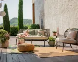 Aménagement terrasse extérieure : un canapé et un fauteuil confortables, des coussins, un plaid coloré, des plantes et des tapis invitent à la détente.