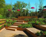 Aménagement de jardins avec terrasses en bois, parterres fleuris et parasols colorés.