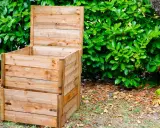 Un composteur en bois, prêt à l'emploi, est installé dans un jardin verdoyant. Idéal pour fabriquer un composteur maison.