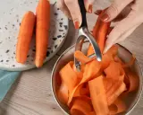 Des carottes épluchées tombent en rubans dans un bol. Une astuce pour comment conserver les carottes : les préparer ainsi pour une cuisson rapide.