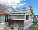 Agrandissement maison sur le côté en cours de construction, murs en parpaings, nouveau toit gris, échafaudage.