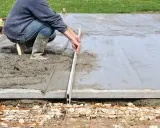 Un ouvrier ajuste le coffrage d'une dalle en béton frais avec une règle de maçon.
