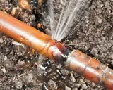 Une fuite sur un tuyau de cuivre, l'eau jaillit d'une fissure dans le sol.