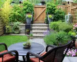 Un petit jardin aménagé avec une table, des chaises, des plantes et une porte en bois.