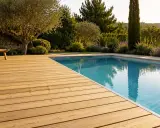 Une belle terrasse bois piscine sans margelle, avec un transat invitant à la détente sous un olivier.