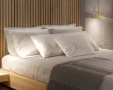 Lit et sa tête de lit en bois, oreillers blancs, lampe dorée. Une ambiance douce pour la deco de chambre.
