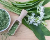 Sel de cuisine à l'ail des ours, avec des feuilles vertes et des fleurs blanches sur fond de bois.