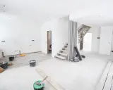 Chantier en cours pour rénover ma maison : escalier, seaux de peinture, balai et matériaux au sol.