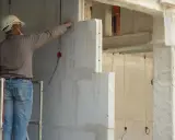 Un ouvrier en casque blanc travaille sur un mur en béton cellulaire, posant des blocs légers.