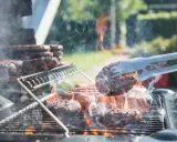 Des hamburgers grillent sur un barbecue à gaz. La cuisson est intense, la fumée s'élève. Nettoyer barbecue gaz après ce festin sera nécessaire.