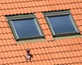 Un chien assis sur une toiture en tuiles, observant le ciel à travers deux fenêtres de toit.
