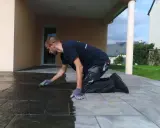 Un homme agenouillé effectue le nettoyage de dalles de terrasse avec une éponge verte, redonnant leur éclat à la pierre.