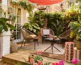Aménager une petite terrasse sans se ruiner : trois fauteuils en rotin, une table basse, des plantes luxuriantes et une toile rouge créent un coin cosy et abordable.