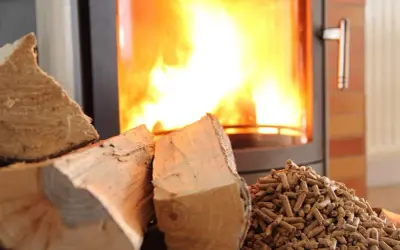Bûches et granulés de bois prêts pour le chauffage au bois, avec un poêle crépitant en arrière-plan.
