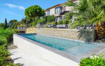 Belle piscine semi enterrée avec un habillage en pierre naturelle, entourée de verdure luxuriante et d'une villa moderne.