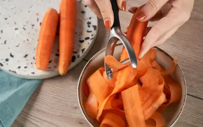 Des carottes épluchées tombent en rubans dans un bol. Une astuce pour comment conserver les carottes : les préparer ainsi pour une cuisson rapide.