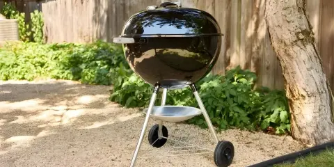 Un barbecue noir fumant, prêt à faire griller de bonnes choses dans le jardin. L'été arrive, il est temps de faire un barbecue !