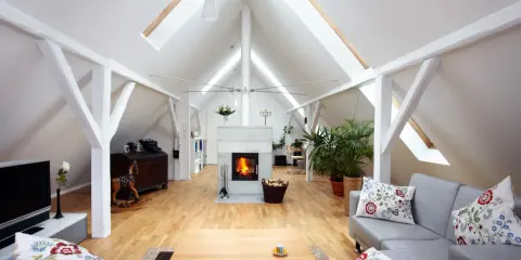Salon aménagé sous les combles avec cheminée, canapés confortables et poutres apparentes. Le cout d'aménagement combles est bien rentabilisé.