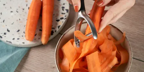 Des carottes épluchées tombent en rubans dans un bol. Une astuce pour comment conserver les carottes : les préparer ainsi pour une cuisson rapide.