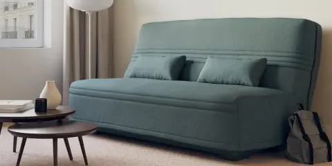 Canapé bz ou clic clac bleu canard, avec coussins, près d'une fenêtre et de tables basses. Parfait pour un petit espace.