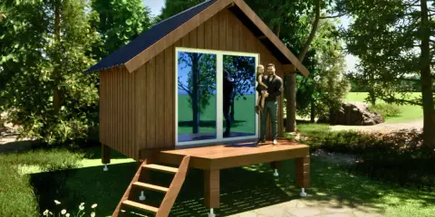 Un homme porte sa fille sur la terrasse d'un abri de jardin sur plot, entouré de verdure.