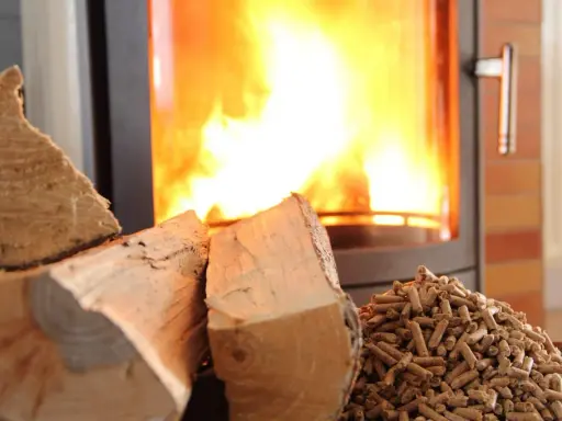 Bûches et granulés de bois prêts pour le chauffage au bois, avec un poêle crépitant en arrière-plan.