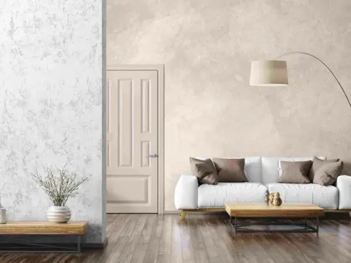 Salon moderne avec un canapé blanc, une table basse en bois et un grand pot de fleurs. Le mur de fond présente un bel **effet enduit décoratif** texturé.