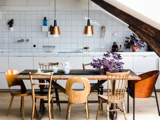 Une cuisine ouverte sur salle à manger avec un îlot central, des chaises en bois et des suspensions cuivrées.