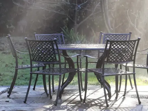 Un ensemble de mobilier de jardin résistant aux intempéries, une table et quatre chaises en métal, est mouillé par la rosée matinale.